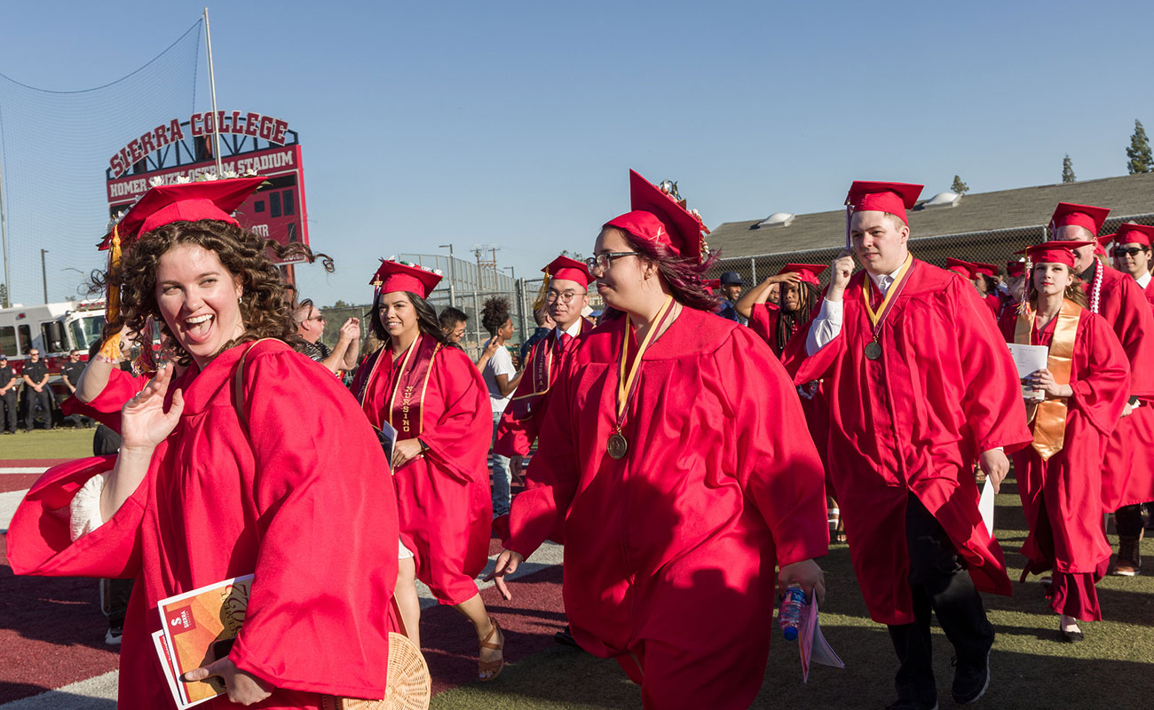 Commencement Grads 2022 walking onto field wearing red caps and gowns