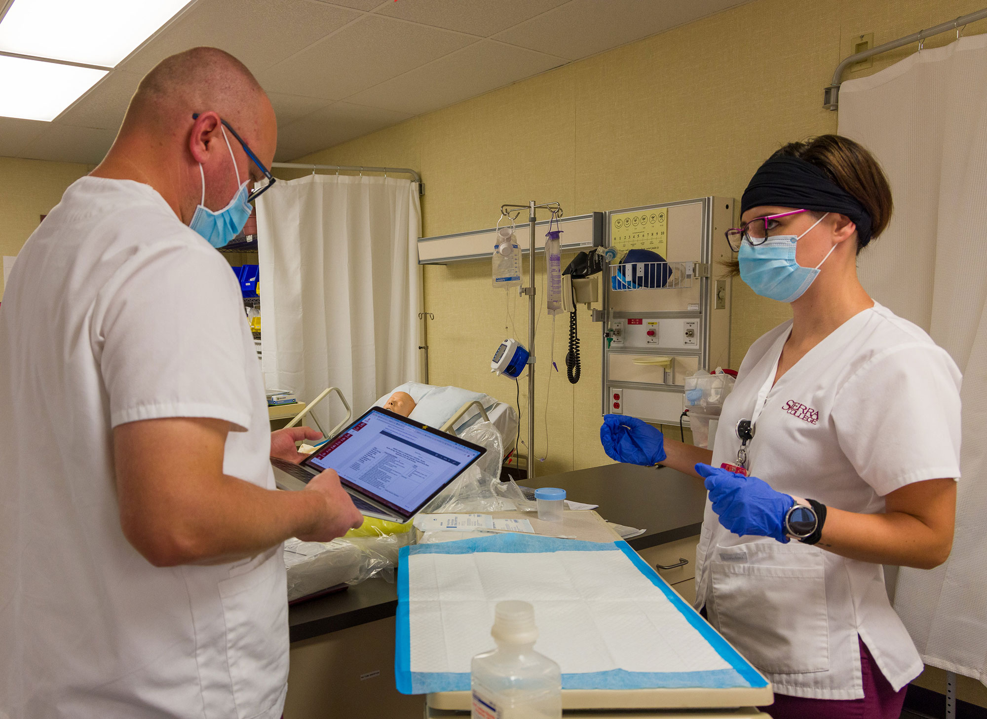 Male nursing student enters clinical information into tablet as female nursing student observes.