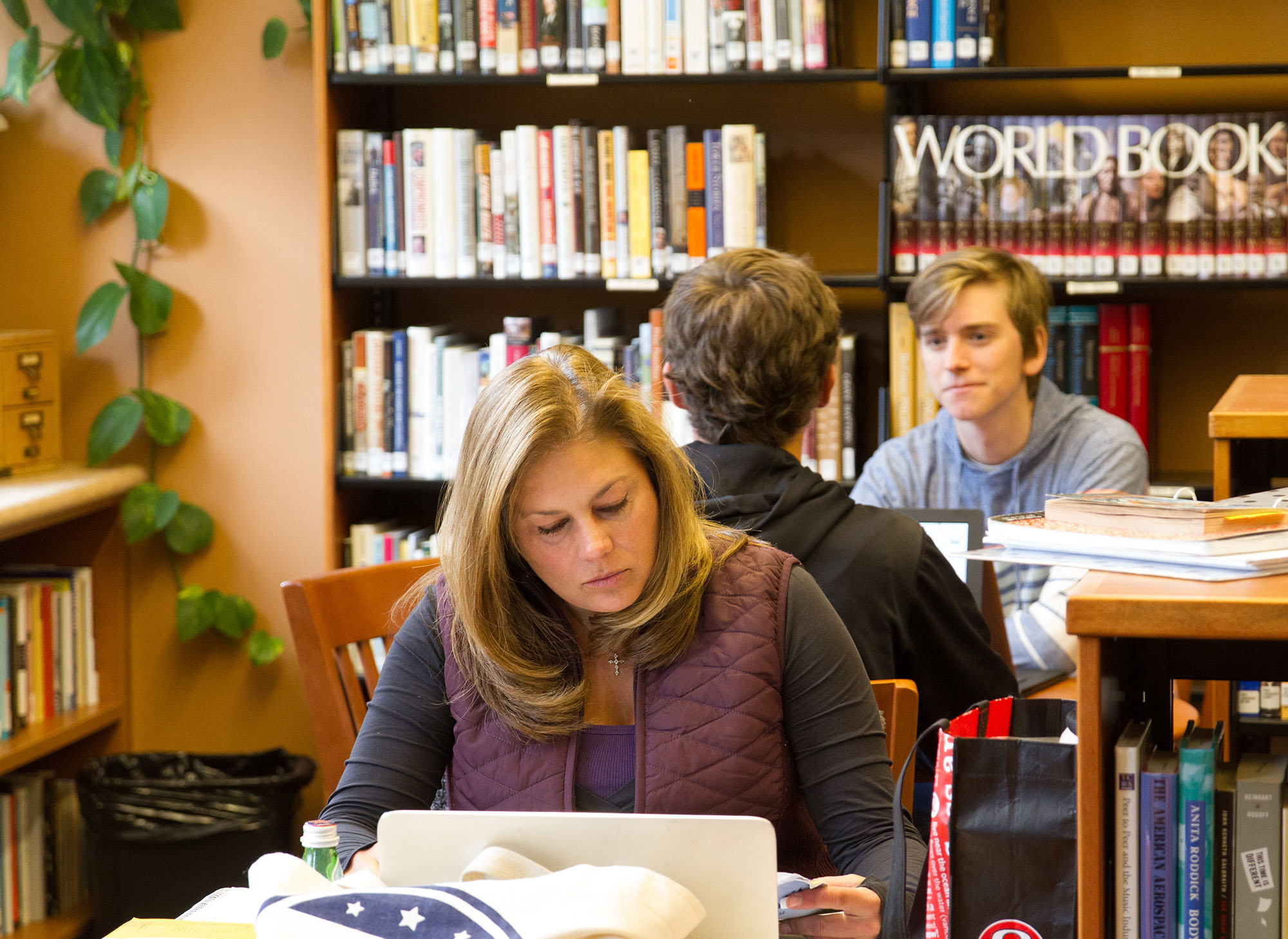 Student studying at the library in front of the World Book Encyclopedia collection