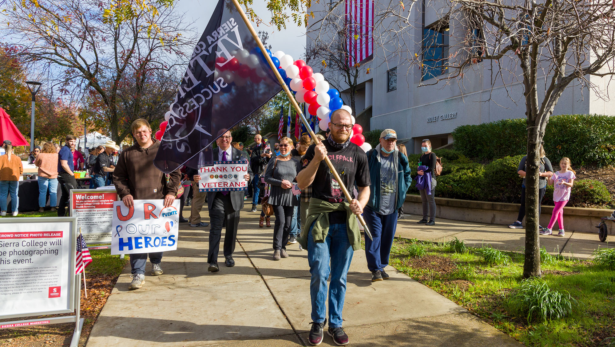 Man holding Veterans Success Center flag while leading a procession around the Sierra College campus during Veterans Day.