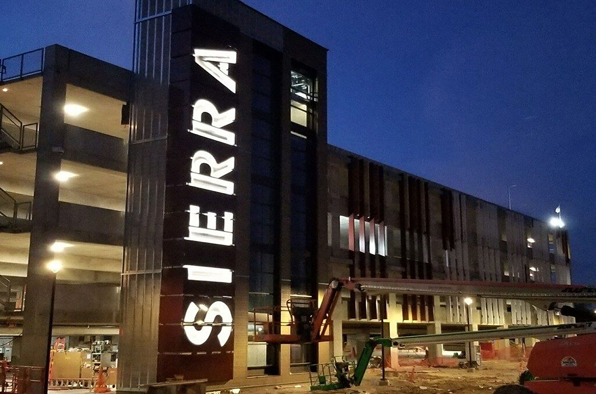 Night picture of construction on new parking garage with large lit up Sierra sign on side of structure.