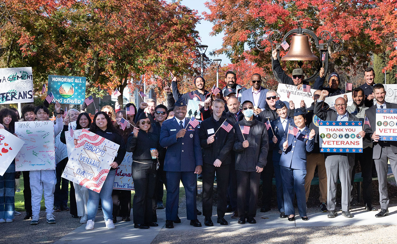 Group of Veterans Day ceremony attendees hold American flags and signs honoring veterans