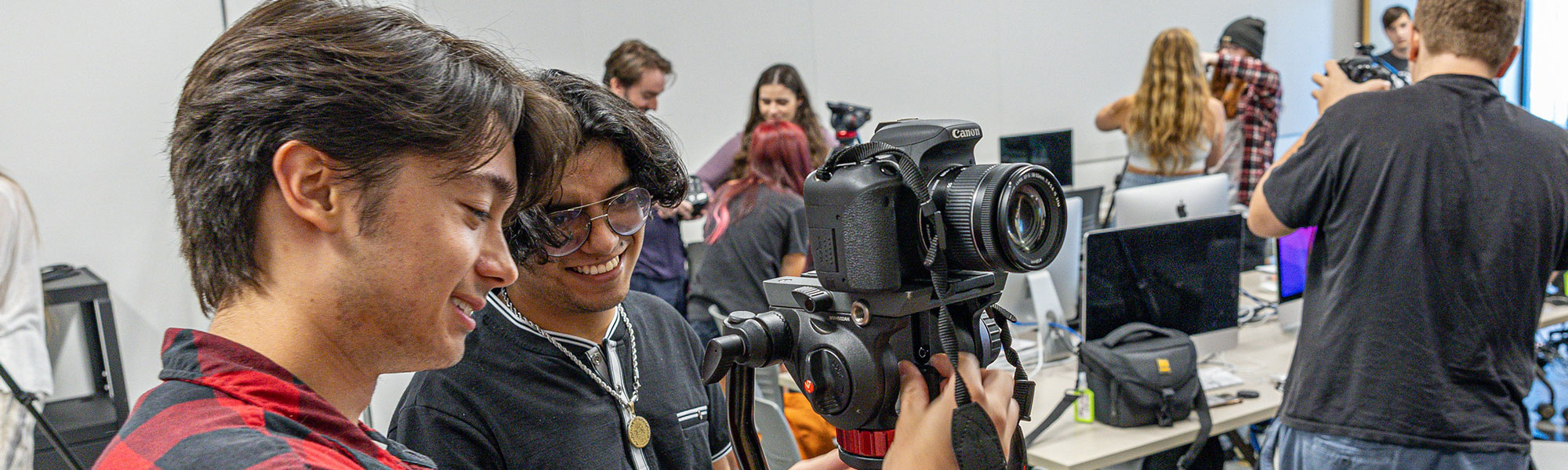 Two students practice using their camera to make movies as other students in classroom do the same.