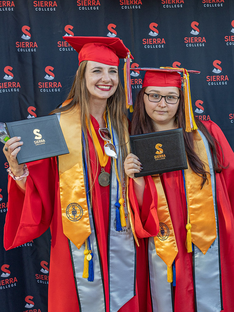 Student wearing graduation cap and gown holding scholarship certificates